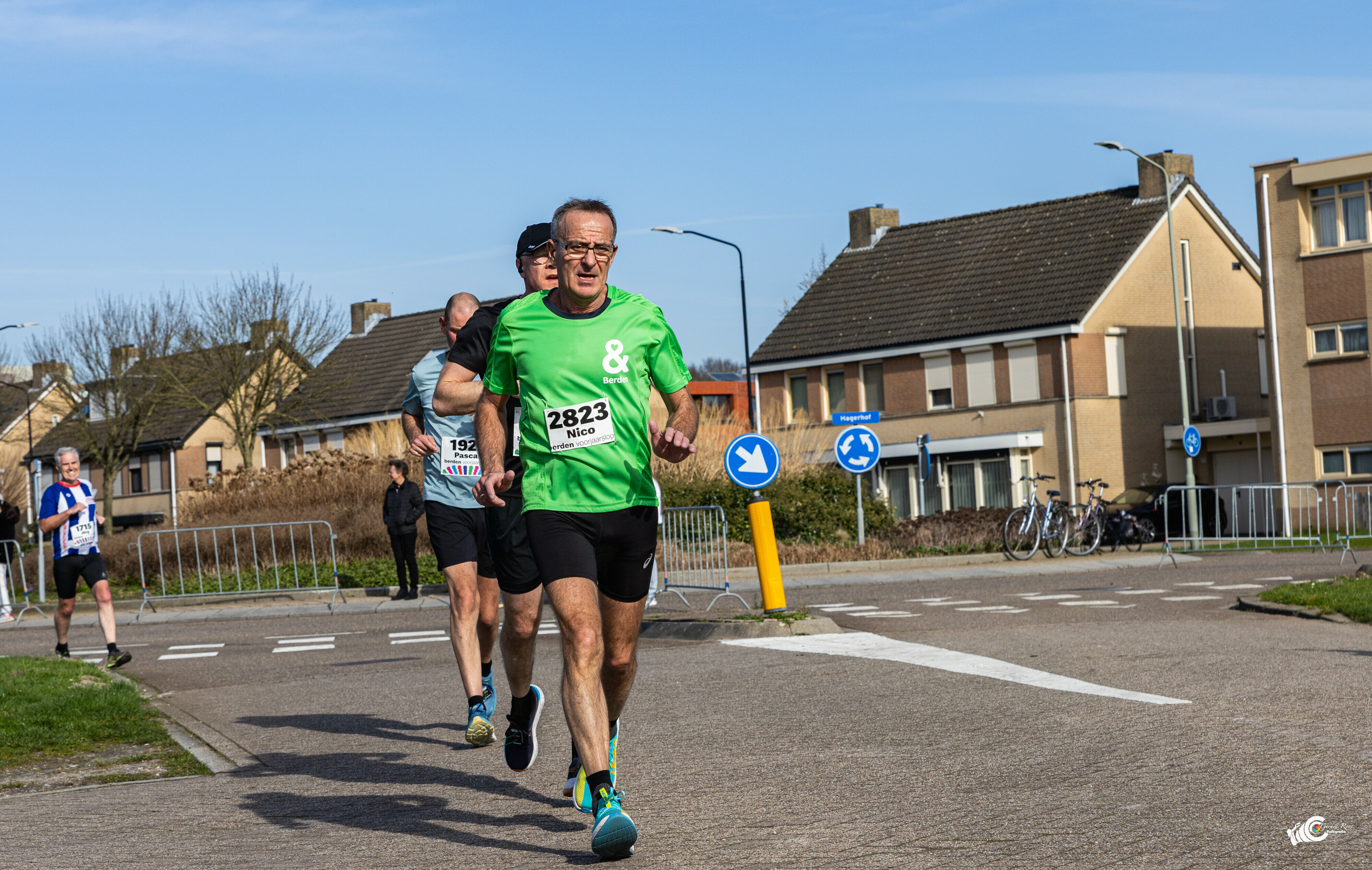 Hardloper met startnummer 2823 in een groen Berden-shirt tijdens de Berden Voorjaarsloop, rennend door een woonwijk op een zonnige dag.